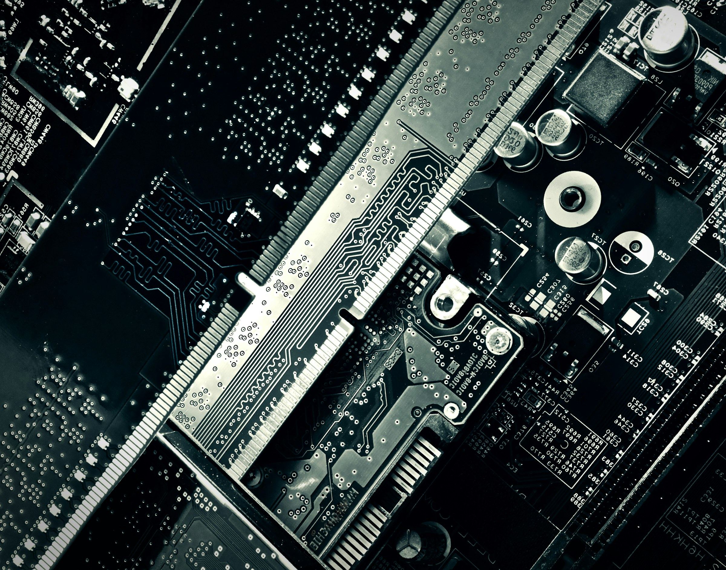 Black and white close-up of a motherboard with a long memory slot running diagonally across capacitors and traces.
