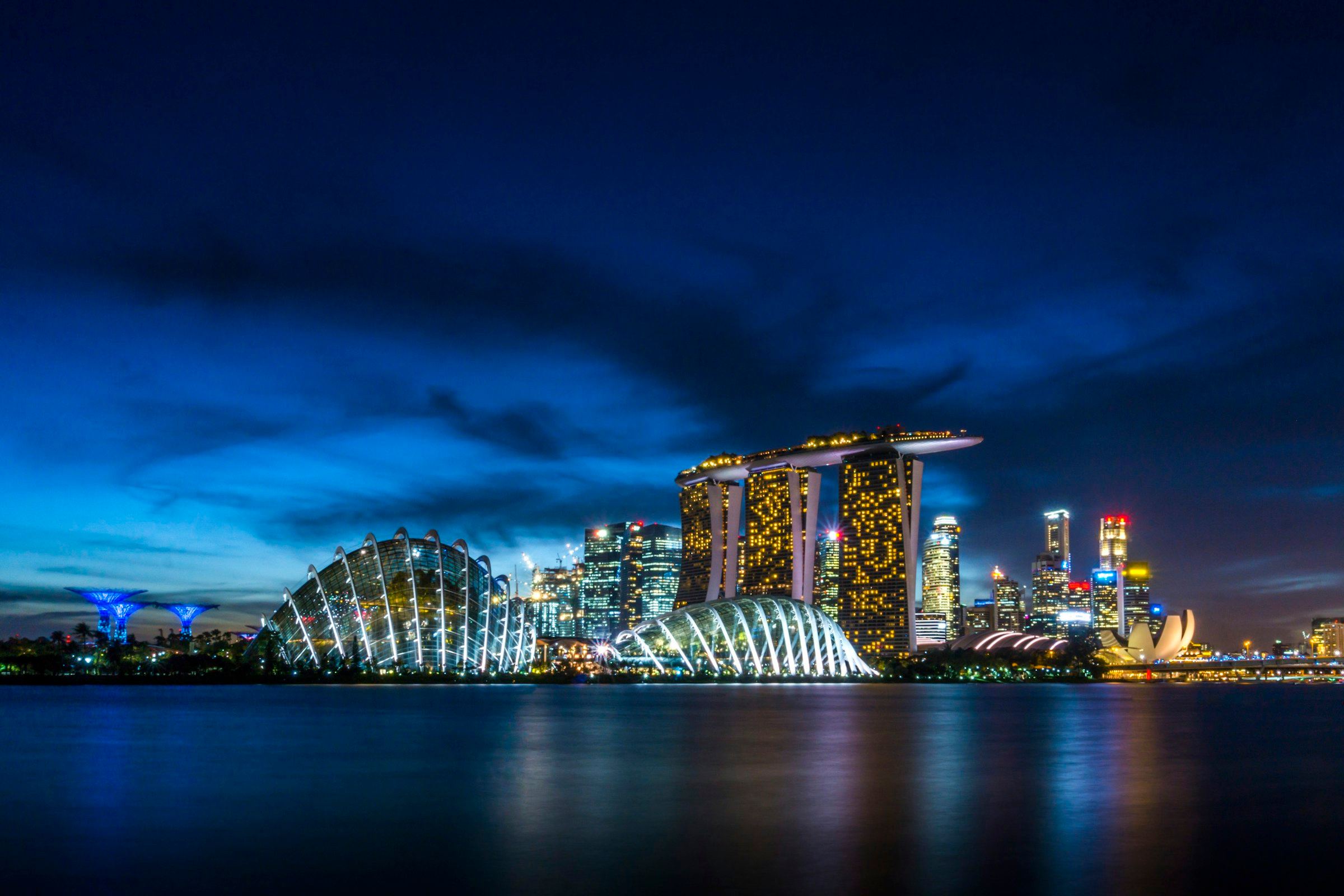 Marina Bay Sands and the Gardens by the Bay domes rise above dark water at blue hour.