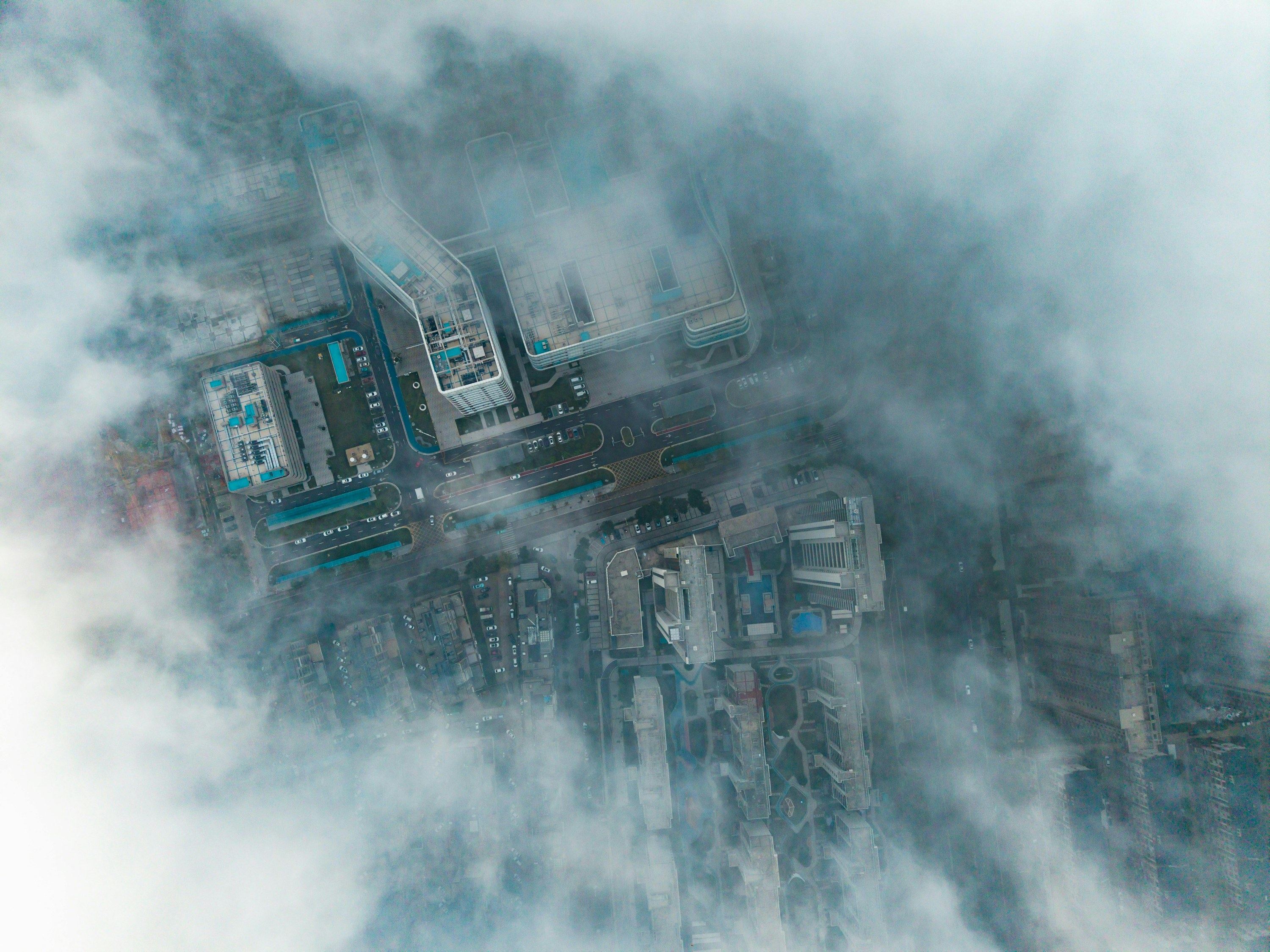 An aerial view of a city block with rooftops and roads partly swallowed by grey cloud.